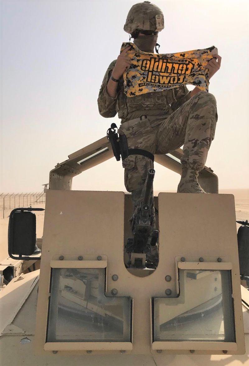 Man sits on M-ATV tank in desert holding Pittsburgh Terrible Towel