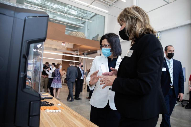 Two individuals stand in front of a 3D printer