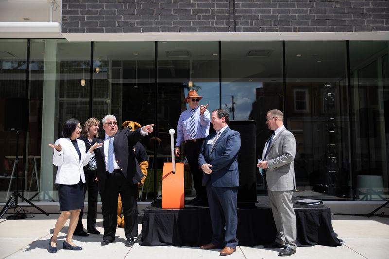 Six individuals stand on and by a stage outside a building