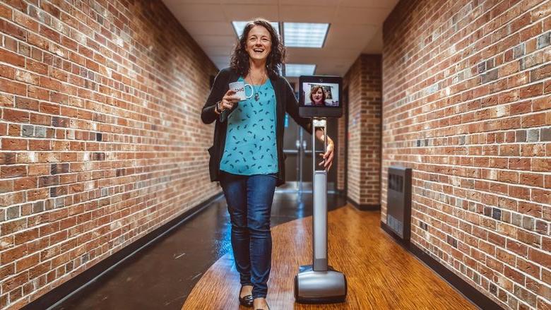 Penelope Morrison walks down a hall with Kristal Tucker projecting herself through the Beam robot