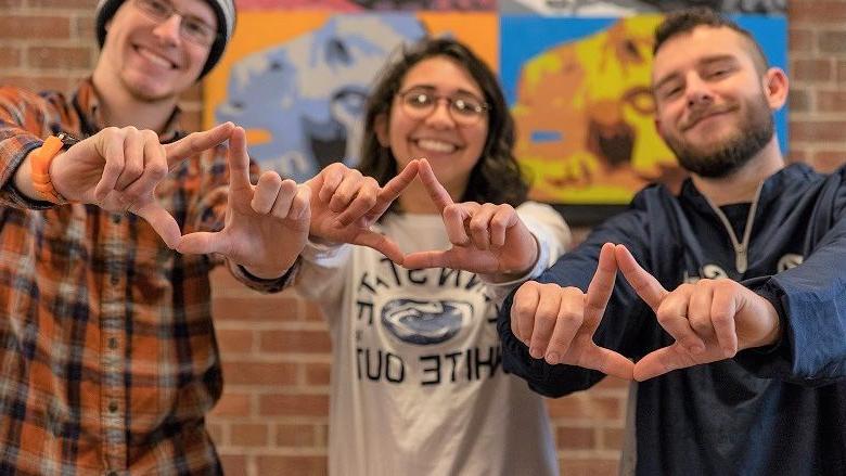 Three students stand with hands shaped like diamonds for THON