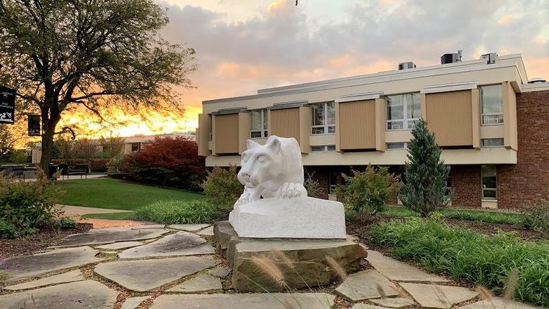 Nittany lion statue in foreground with campus buildings in background