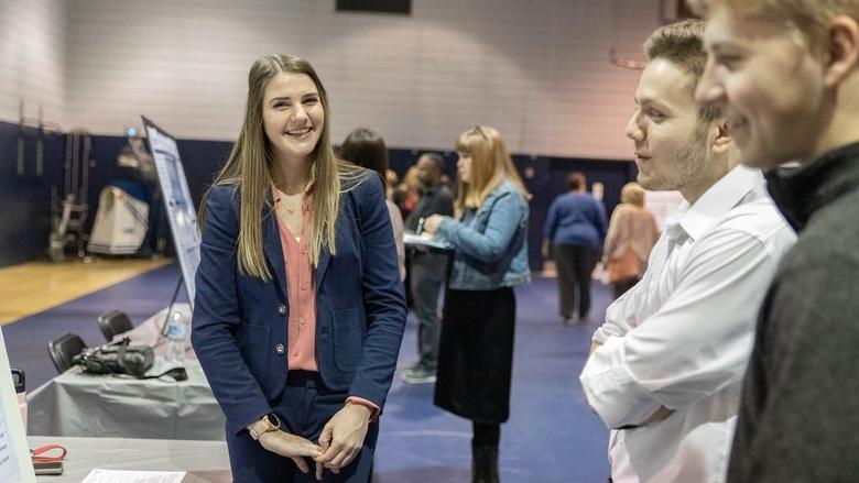 Female student smiles as two male students look at research poster