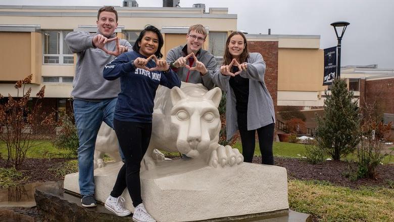 Four students stand by lion statue