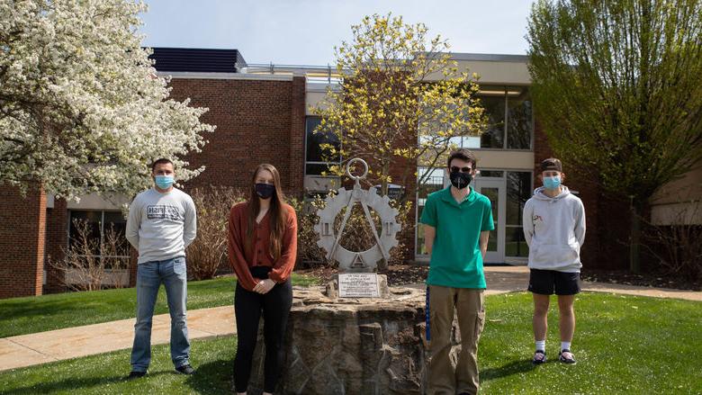 Four students stand outside by statue