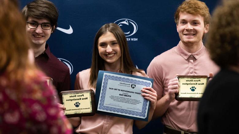 Three students smile to take photo while holding awards