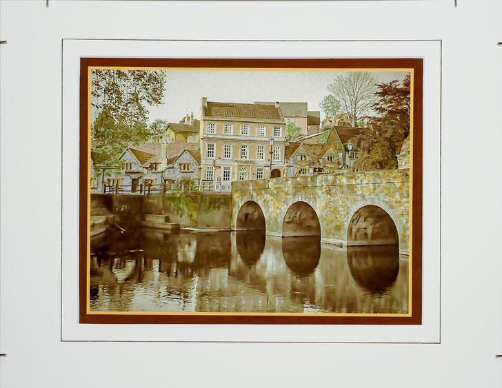 Hand-colored, monochrome photograph of stone bridge and building by Frank Santimauro