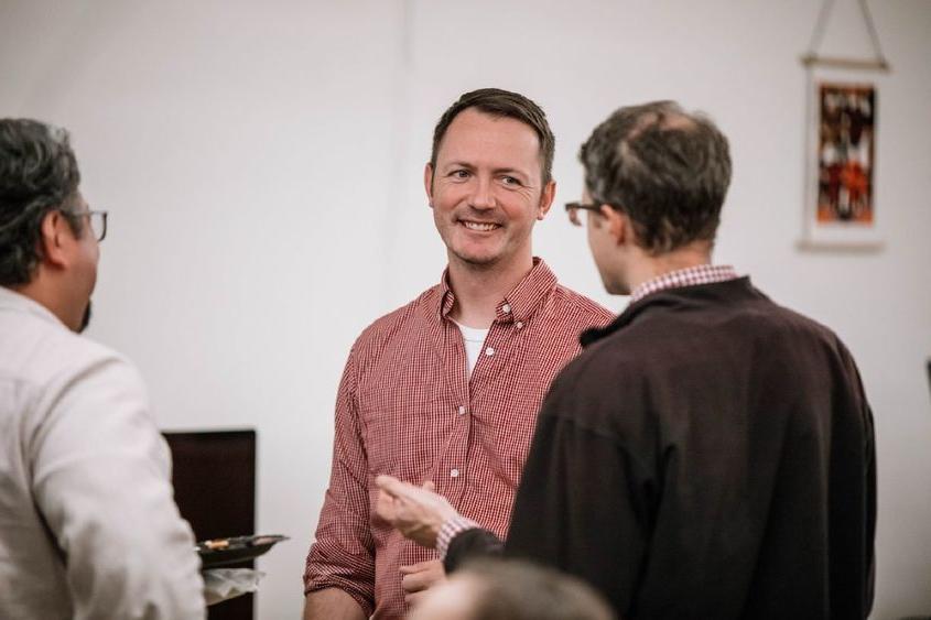 Man smiles as another man talks