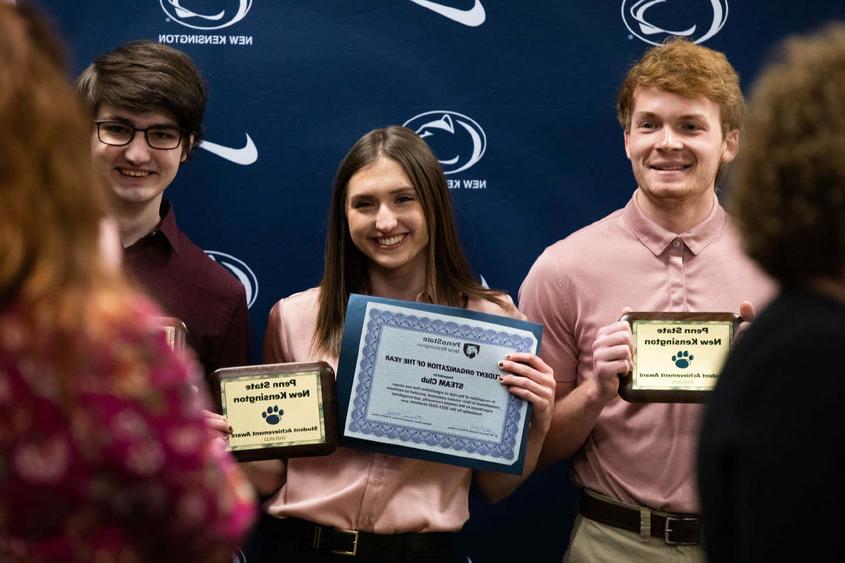 Three students smile to take photo while holding awards